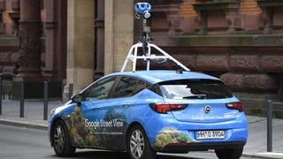 Ein Wagen von Google Street View fährt mit einer Kamera auf dem Dach durch die Stadt. 