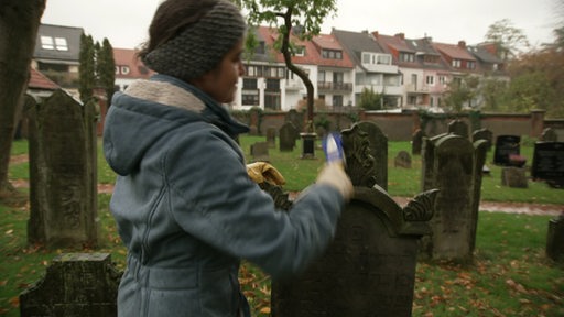 Frau säubert Grabstein auf Friedhof mit Bürste
