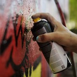 Ein Mann sprueht mit einer Spraydose ein Graffiti an eine Wand. 