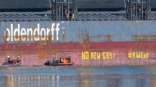 Zwei Schlauchboote von Greenpeace fahren an einem Schiff entlang. Aktivisten haben zwei Botschaften an das Schiff gemalt.