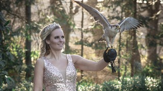 Eine Frau in einem Kleid hält einen Greifvogel auf der Hand.