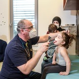 Ein Arzt mit Maske schaut einem Kind in den Hals.