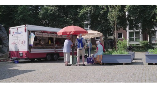 Einige Menschen stehen unter Schirmen um einen mobilen Marktstand herum