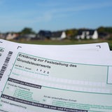 Ein Erklärung zur Feststellung des Grundsteuerwerts für das Jahr 2025 wird vor eine Wohnsiedlung hochgehalten.