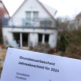 Ein Grundsteuerbescheid für 2024 wird vor einem Privatgrundstück gehalten. 