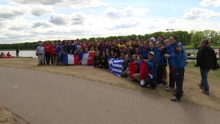 Viele Schüler unterschiedlicher Nationen posieren für ein Gruppenfoto am Werdersee, einige halten Flaggen hoch.