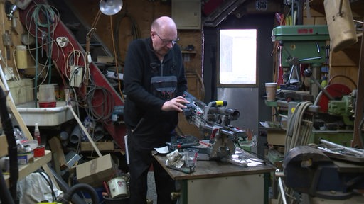 Günther steht in seiner Werkstatt und repariert Werkzeuge. 