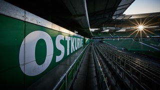 Blick auf die leeren Ränge des Weser-Stadions und den weißen Schriftzug "Ostkurve" bei Sonnenuntergang.