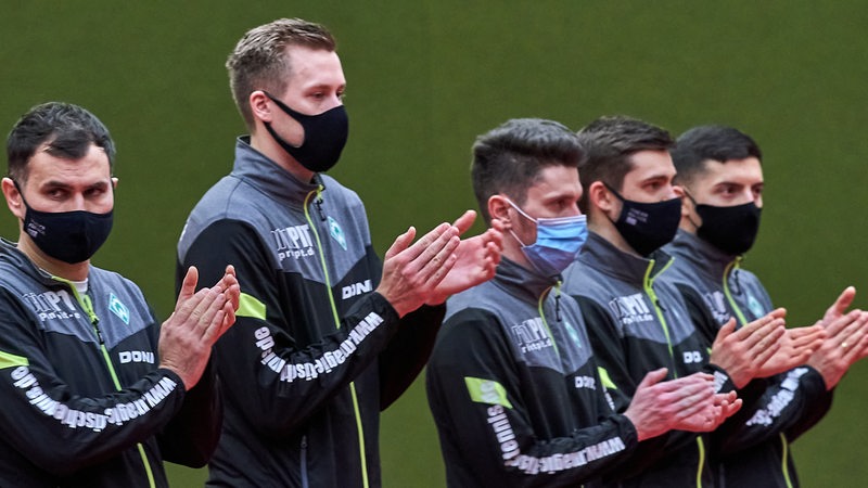 Werders Tischtennis-Team aus Trainer Tamas, Falck, Szöcs, Gerassimenko und Aguirre steht mit Masken nebeneinander und applaudieren dem Gegner bei der Vorstellung.