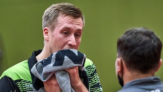 Werders Tischtennis-Profi Mattias Falck wischt sich bei der Auszeit im Gespräch mit Trainer Cristian Tamas frustriert mit dem Handtuch durchs Gesicht.