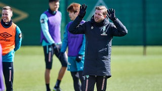 Werder-Coach Florian Kohfeldt reckt beim Training beide Hände hoch, um etwas zu erklären.