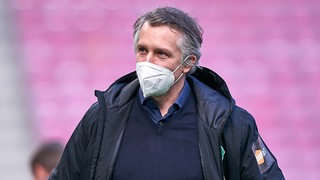 Werder-Sportchef Frank Baumann mit einer weißen Mund-Nase-Maske auf dem Weg zur Trainerbank.