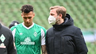 Florian Kohfeldt trägt einen Mund-Nasen-Schutz und spricht nach dem Leipzig-Spiel auf dem Rase mit Davie Selke, der in Richtung Boden blickt.