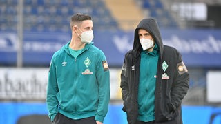 Die Werder-Spieler Marco Friedl und Maximilian Eggestein tragen beide weiße FFP2-Masken, als sie in Bielefeld die Platzbegehung machen.