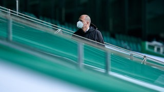 Werders Finanzchef Klaus Filbry steht mit weißer FFP2-Maske alleine auf einer grünen Tribüne im Weser-Stadion.