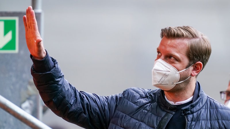Werder-Trainer Florian Kohfeldt winkt mit aufgesetzter FFP2-Maske Richtung Tribüne im Augsburger Stadion.