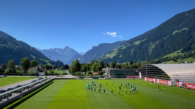 Blick auf Werders Trainingsplatz in Zell am Ziller vor dem Alpenpanorama bei strahlendem Sonnenschein und blauem Himmel.