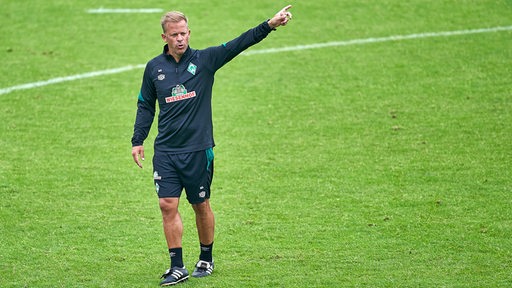 Werder-Training Markus Anfang ruft über den Trainingsplatz und streckt den Arm aus.