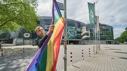 Ein Mitarbeiter von Werder Bremen hängt vor dem Weserstadion zwischen den Werder-Fahnen eine Regenbogenflagge auf.