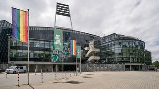 Vor dem Bremer Weserstadion wehen im Sonnenlicht zwischen den Werder-Flaggen auch Regenbogen-Fahnen.