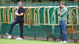 Werder-Sportchef Frank Baumann und Clemens Fritz stehen telefonierend am Trainingsplatz.