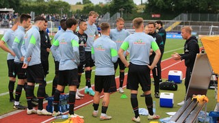 Werder-Trainer Markus Anfang erklärt an der Taktiktafel am Spielfeldrand seinen Spielern etwas, die ihn umringen.