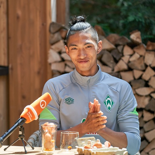Werder-Profi Kyu-Hyun Park reibt sich grinsend die Hände, nachdem er vor der Kamera sechs rohe Eier getrunken hat.