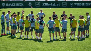 Werder-Trainer Markus Anfang steht auf dem Trainingsplatz im Zillertal umringt von seinen Spielern und erklärt etwas.