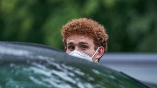 Werder-Profi Joshua Sargent beim Verlassen des Weserstadions mit weißer Maske vor seinem Auto.