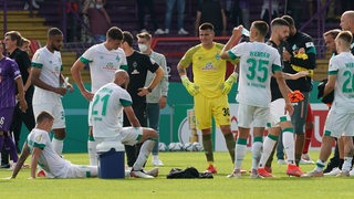 Enttäuschte Werder-Spieler stehen und sitzen nach dem Pokal-Aus auf dem Spielfeld im Kreis herum.