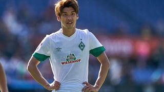 Werder-Profi Yuya Osako stützt auf dem Spielfeld nachdenklich die Hände in die Hüften.