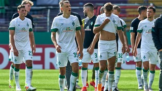 Enttäuschte Werder-Spieler stehen nach dem Pokal-Aus verloren auf dem Rasen.