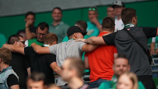 Mehrerer Werder-Fans wenden sich Arm in Arm vom Spielfeld ab.
