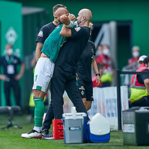 Werder-Kapitän Ömer Toprak wird an der Seitenlinie vom Physiotherapeuten im Stehen der Rücken eingerenkt.