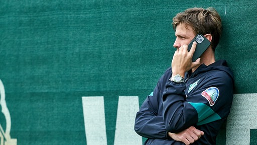 Clemens Fritz telefoniert am Rande des Trainings und lehnt dabei am Zaun.