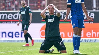 Werder-Spieler Marco Friedl kniet nach verpasster Torchance auf dem Rasen und fährt sich frustriert durch die Haare.