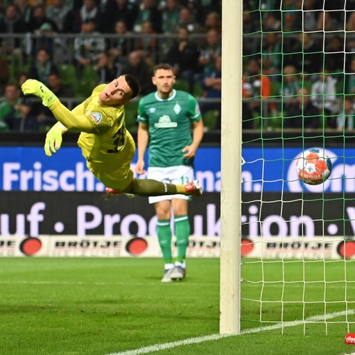 Werder-Torwart Michael Zetterer schaut im Flug waagerecht in der Luft, dem Ball hinterher, der ins Tor fliegt.