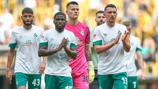Mehrere Werder-Spieler gehen enttäuscht vom Platz und applaudieren ihren Fans.