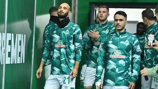 Werder-Spieler um Ömer Toprak kommen vor dem Spiel mit ernsten Mienen aus dem Spielertunnel im Weserstadion.