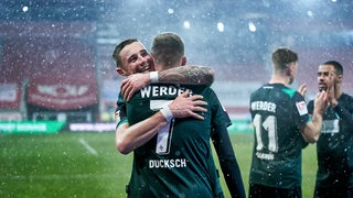 Die Werder-Spieler Marco Friedl und Marvin Ducksch umarmen sich nach dem Sieg in Regensburg bei leichtem Schneefall.