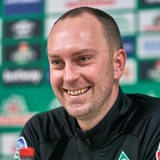 Werder-Trainer Ole Werner grinst während einer Pressekonferenz.