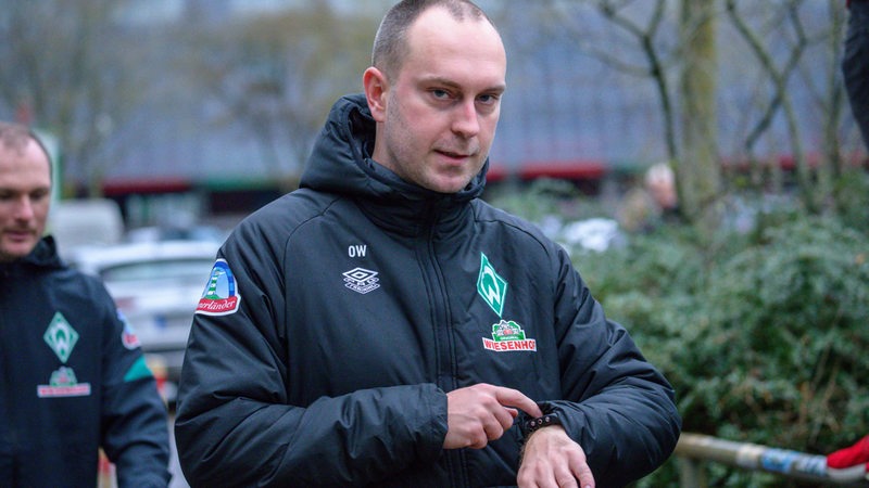 Werder-Trainer Ole Werner schaut auf dem Weg zum Trainingsplatz auf seine Armbanduhr.
