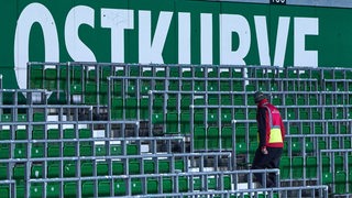 Ein Ordner schreitet die leeren Ränge der Ostkurve im Weser-Stadion ab.