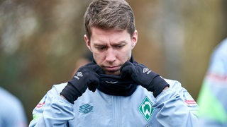 Werder-Profi Mitchell Weiser zieht sich auf dem Weg zum Trainingsplatz den schwarzen Schal zurecht.