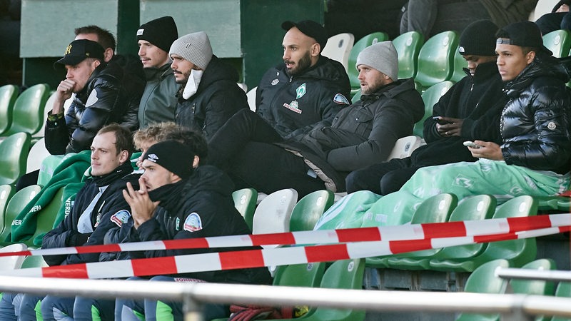 Werder-Stammspieler sitzen im Stadion Platz 11 auf der Tribüne und verfolgen ein Testspiel der Reservisten gegen Zwolle.