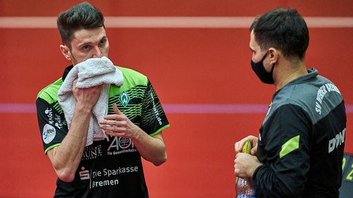 Werders Tischtennis-Coach Cristian Tamas spricht während einer Auszeit mit Hunor Szöcs, der sich mit einem Handtuch das Gesicht wischt.