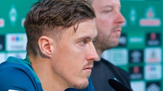 Max Kruse und Werder-Trainer Florian Kohfeldt sitzen nebeneinander auf dem Podium bei einer Pressekonferenz.