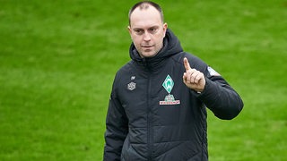Werder-Trainer Ole Werner reckt während des Trainings den Finger hoch.