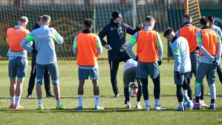 Ole Werner steht beim Werder-Training umringt von seinen Spielern und erklärt etwas.