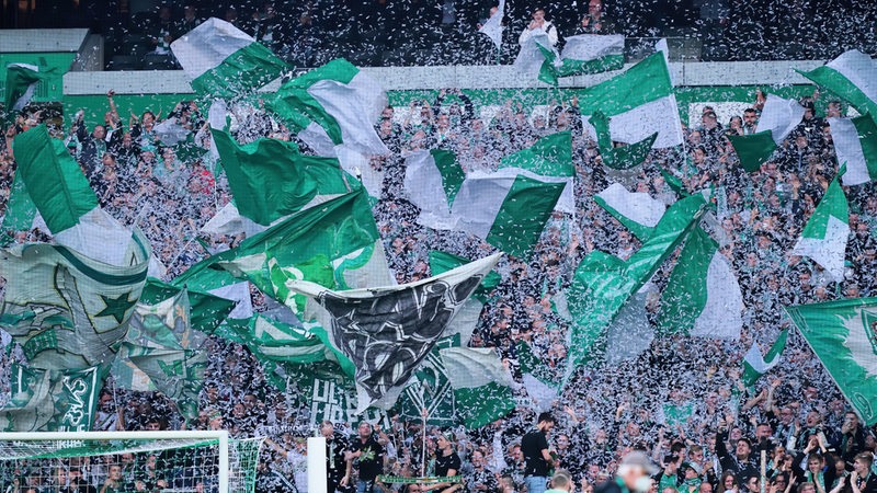 In der Ostkurve werfen die Werder-Fans weiße Papierschnipsel in die Luft und schwenken ihre Fahnen.